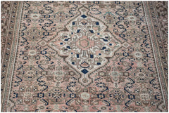 A vintage handwoven Persian rug featuring a central medallion in muted pink, blue, and brown tones.