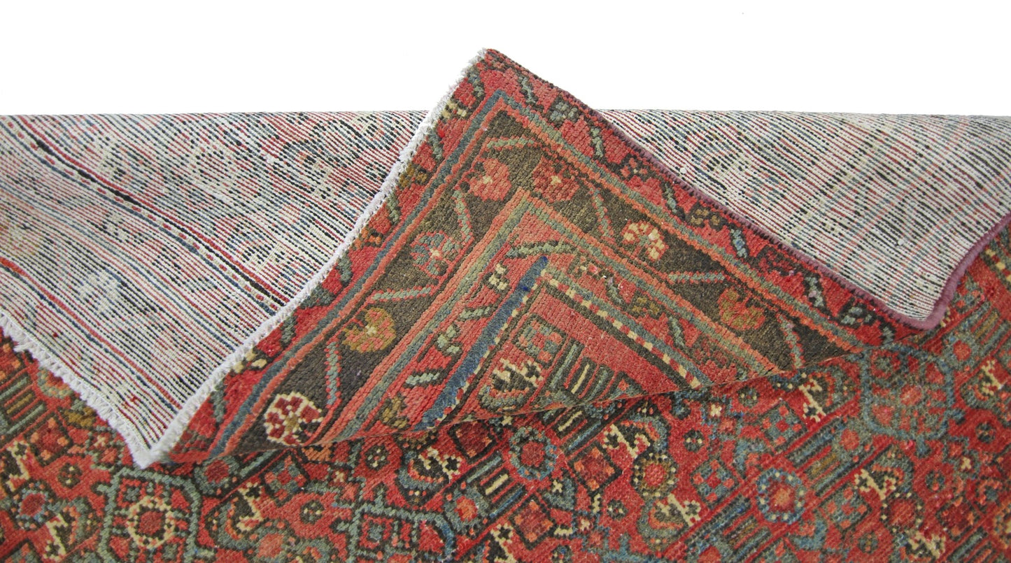 A vintage handmade Persian rug with a red and blue geometric pattern, shown folded to reveal backing.