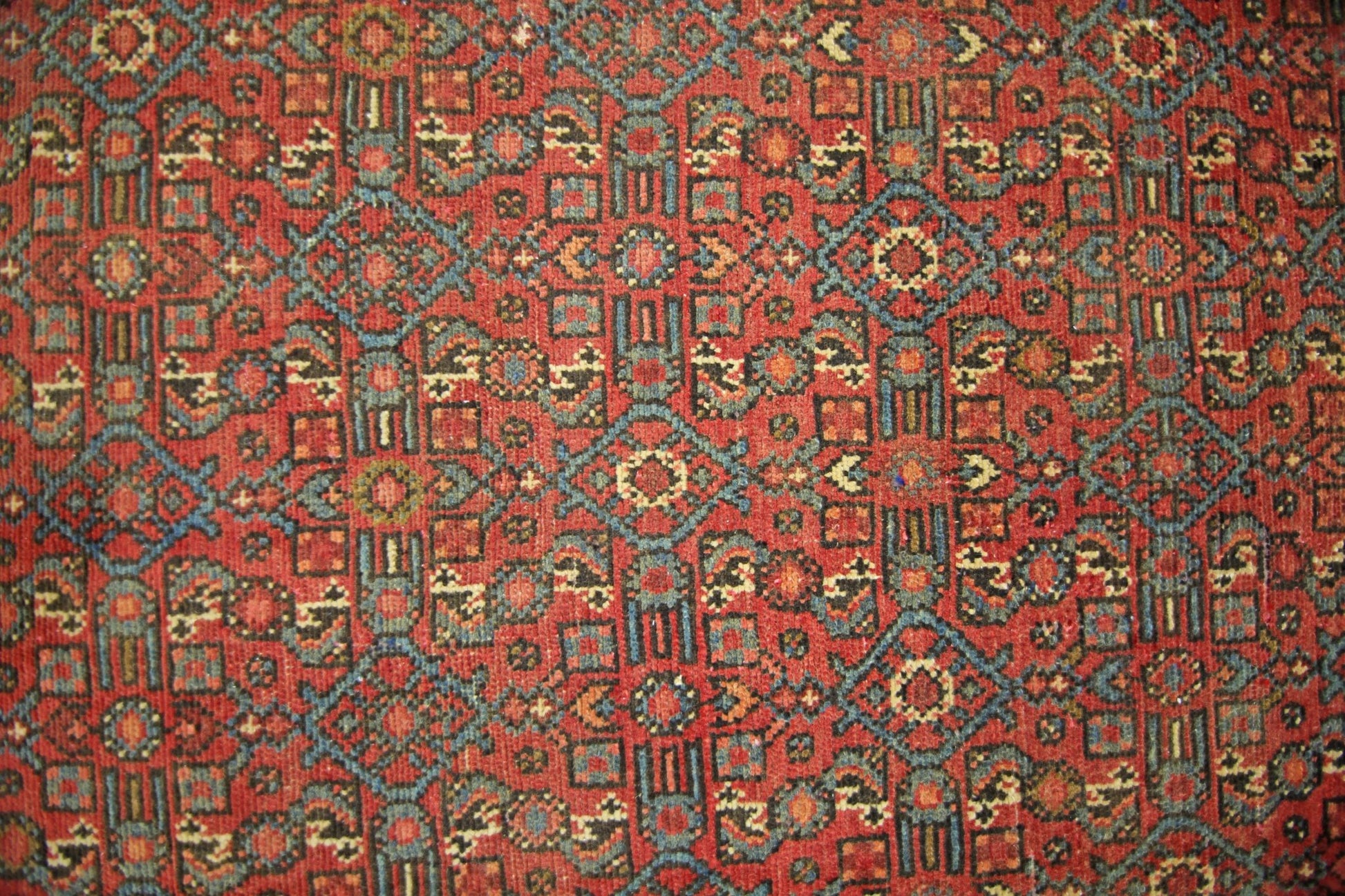 A vintage Persian rug featuring a geometric pattern in shades of red, blue, and cream.