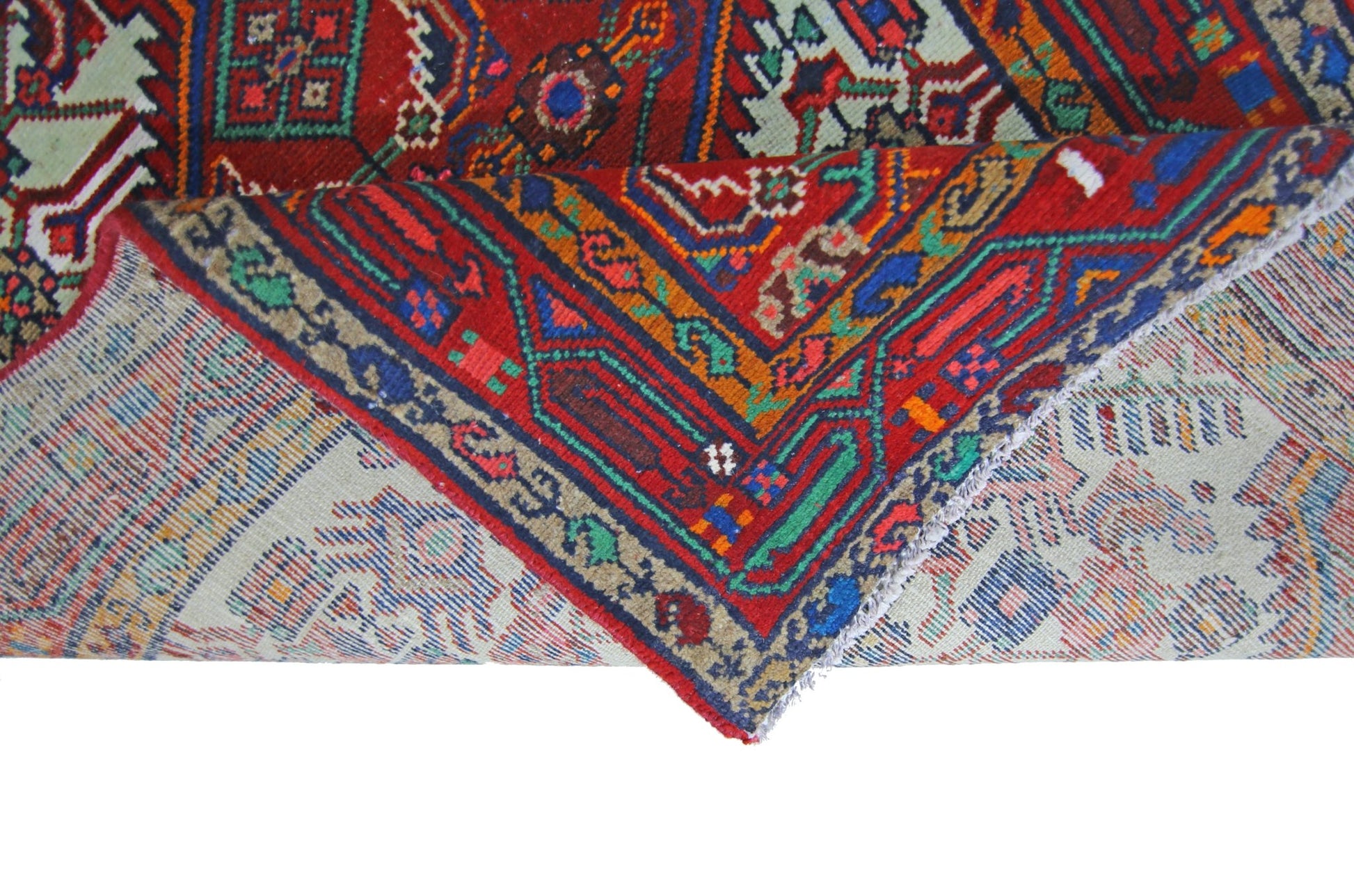 A vintage Persian Hamadan runner with a folded corner revealing its intricate red, blue, and green geometric patterns.