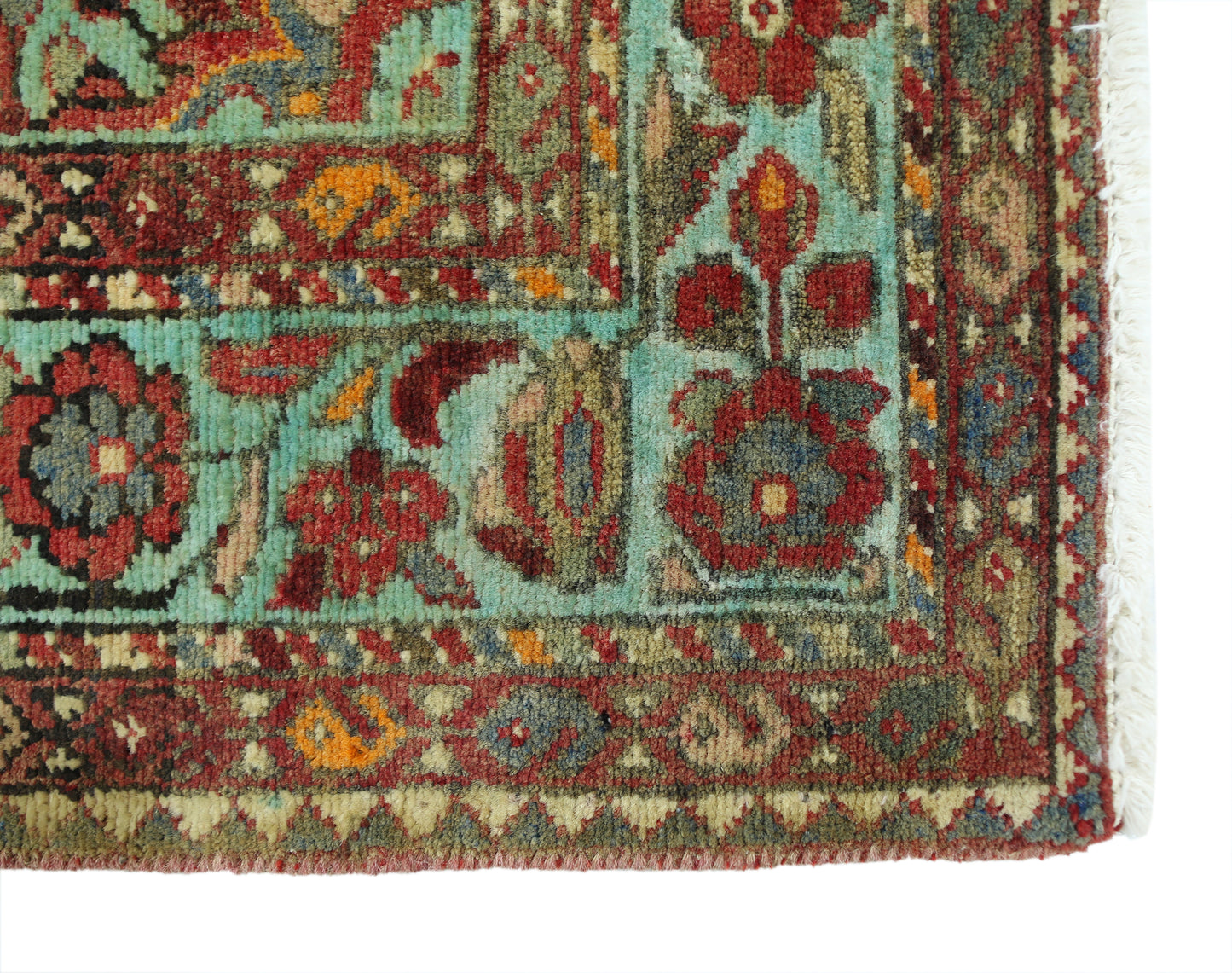 A corner detail of a vintage Persian Hossainabad runner featuring intricate floral patterns in red, blue, and green wool.