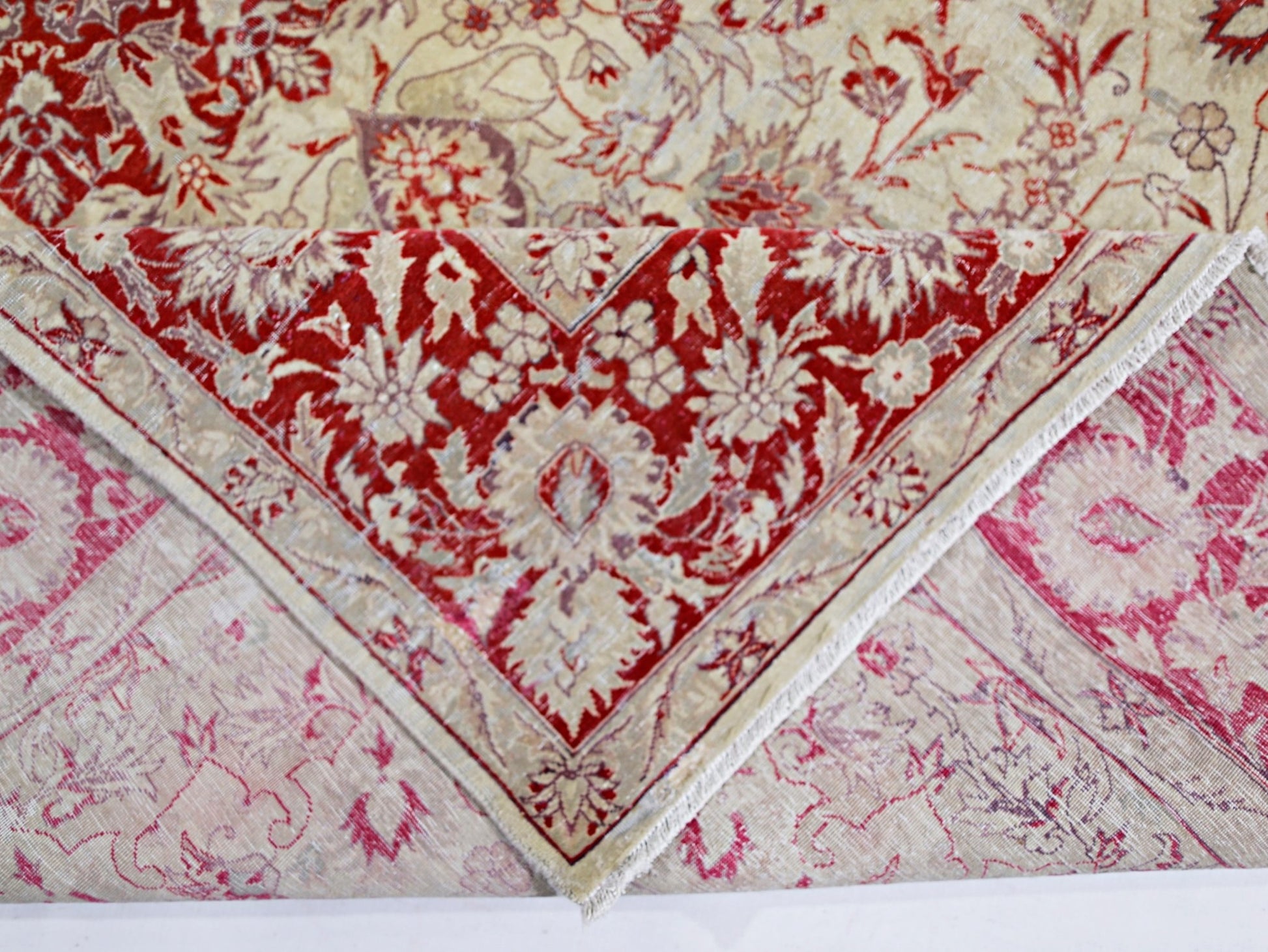 A vintage handmade Pakistani rug featuring a red and cream floral pattern folded to show its back.