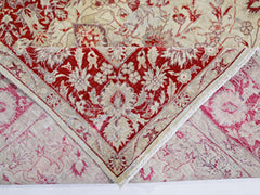 A vintage handmade Pakistani rug featuring a red and cream floral pattern folded to show its back.
