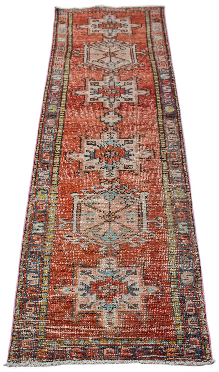 A vintage handwoven Persian Karaja runner rug featuring geometric medallions on a rust red field.