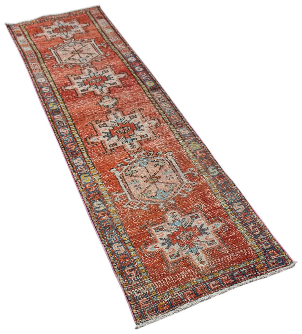A vintage Persian Karaja runner rug featuring geometric medallions on a distressed red field.