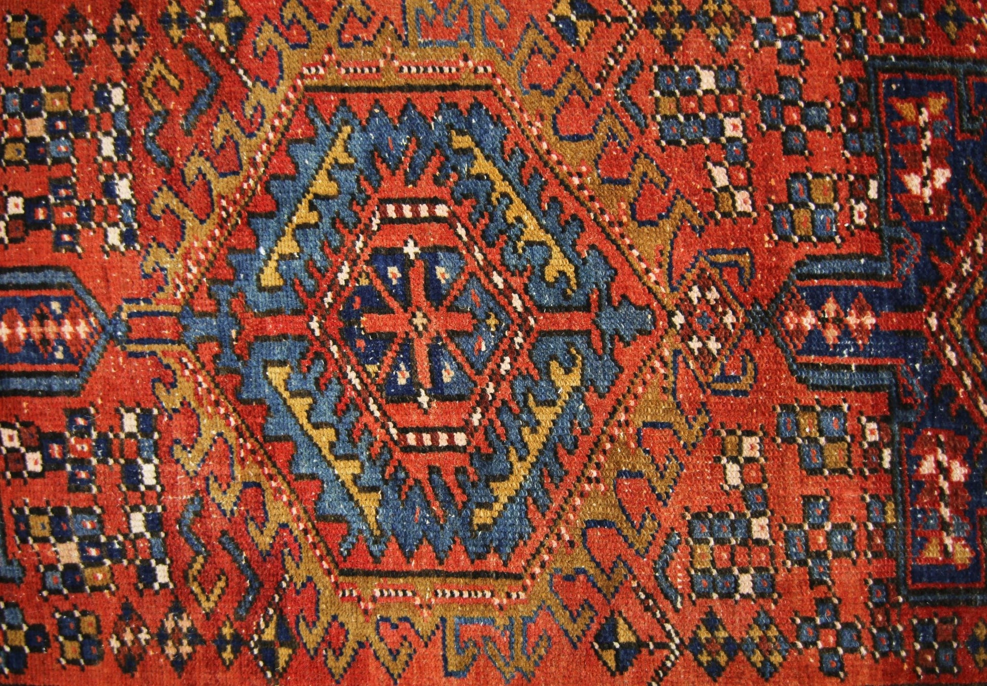 A vintage Persian Karaja runner featuring a geometric medallion pattern in red, blue, and gold.