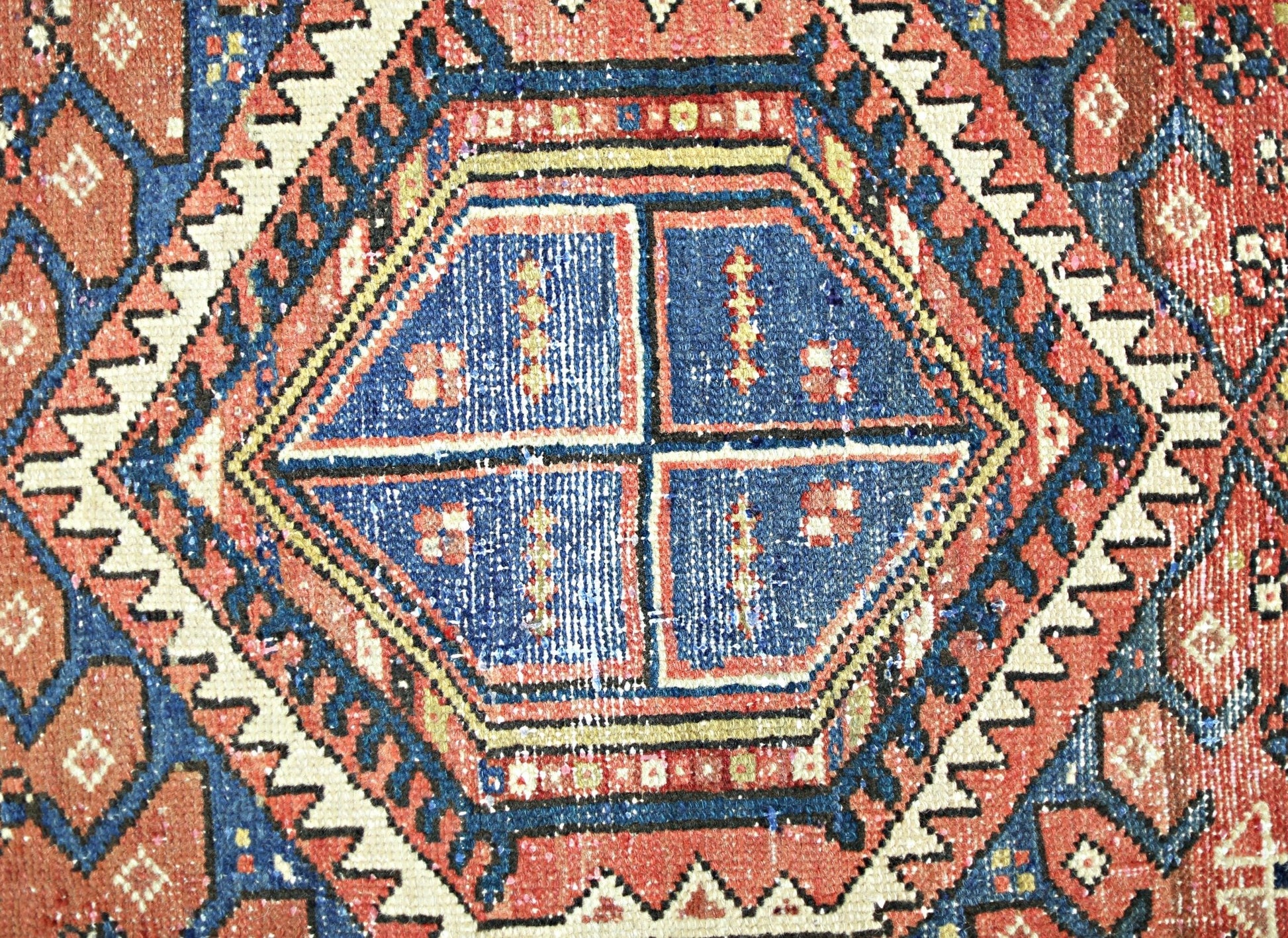 A close-up of a vintage Persian Karaja runner featuring a geometric blue medallion on a red field.