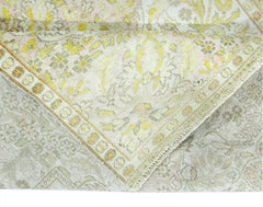 A folded vintage Persian Kashan rug featuring a floral pattern in soft yellow and cream tones.