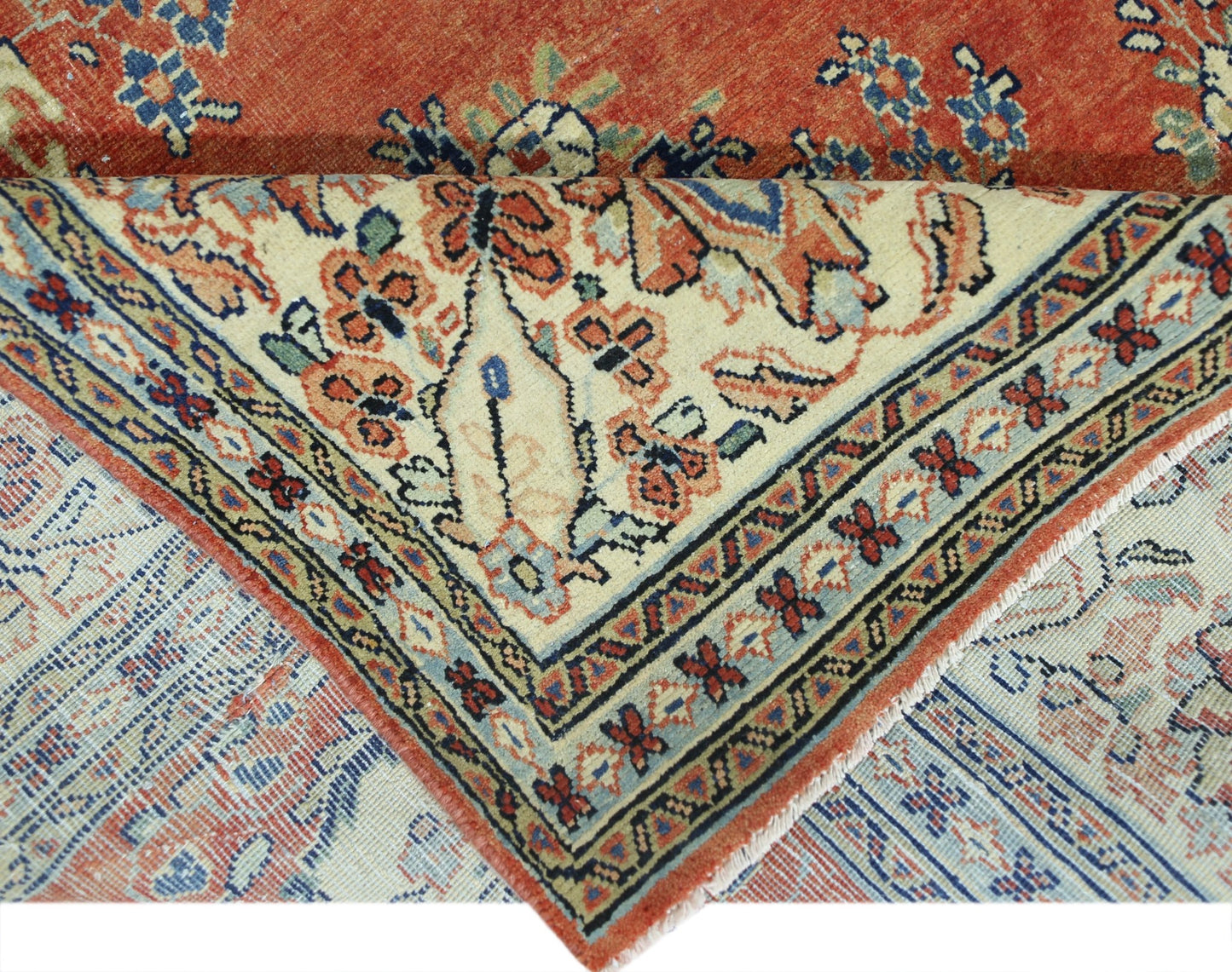 A vintage Persian Tabriz rug with a floral pattern, shown folded to reveal its woven underside.
