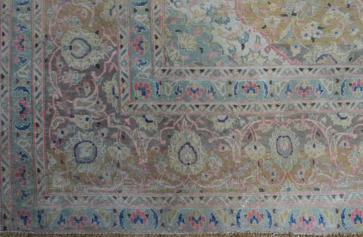 A vintage Persian Kashan rug featuring intricate floral patterns in muted pink, blue, and gold tones.