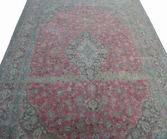 A vintage Persian Kashan rug featuring intricate floral patterns in pink, grey, and blue tones.