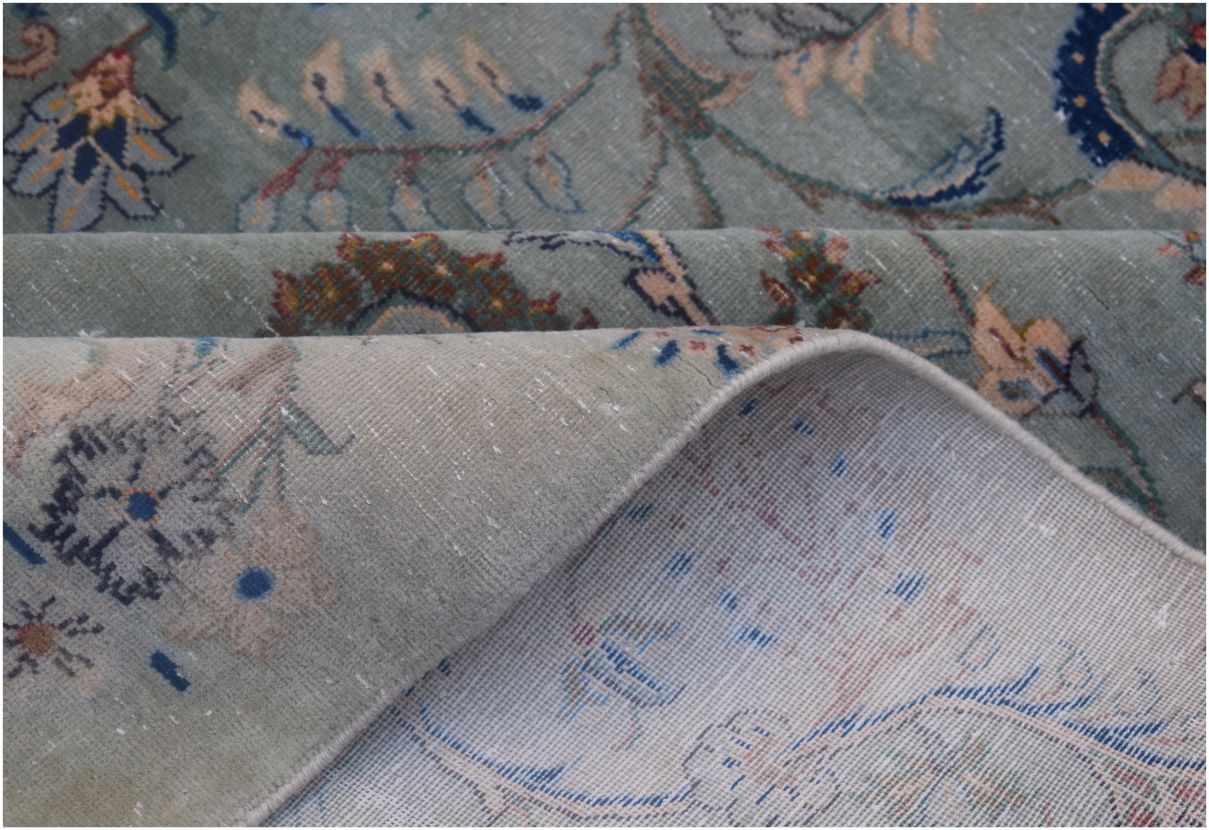 A vintage Persian Kashan rug with a sage green floral pattern and a visible cotton foundation.