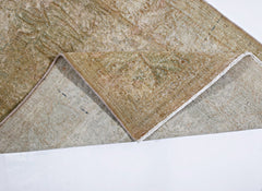 A corner of a vintage Persian Kerman rug is folded back to show its intricate floral pattern.
