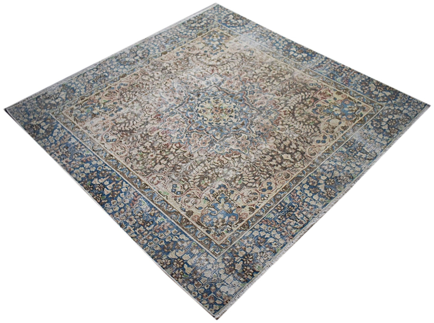 A vintage Persian Kerman rug featuring an intricate floral medallion in blue and beige tones.