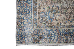 A vintage Persian Kerman rug featuring an intricate floral pattern in blue, brown, and cream tones.