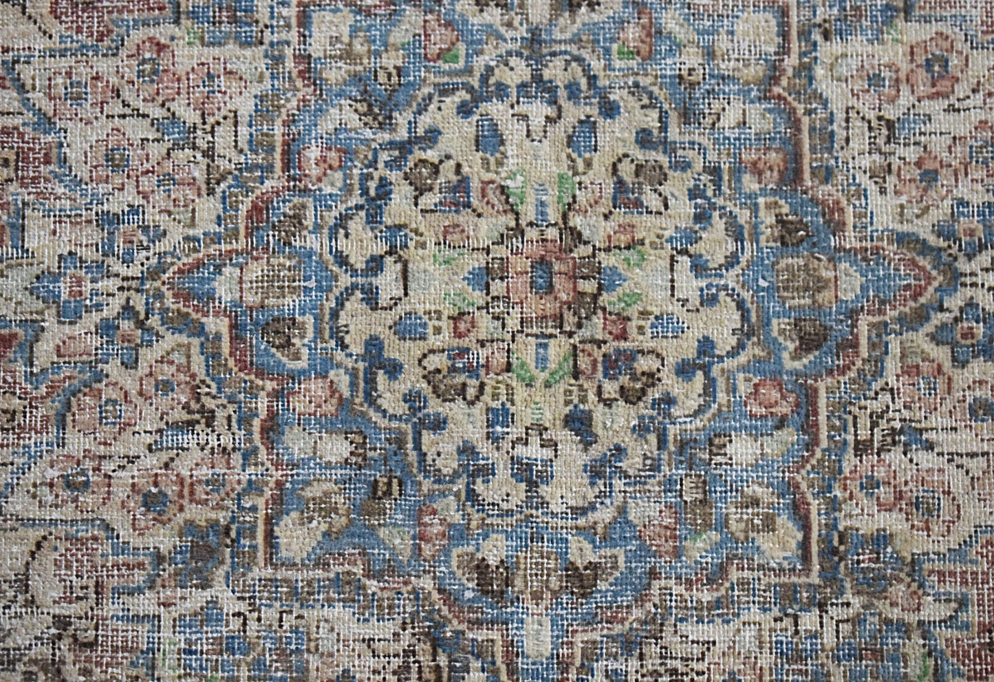A vintage Persian Kerman rug featuring an intricate floral medallion in blue, cream, and red tones.