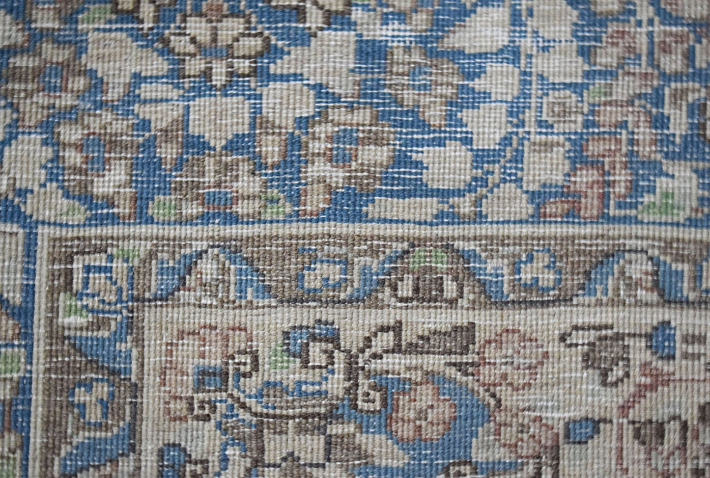 A close-up view of a vintage Persian Kerman rug featuring intricate floral patterns in blue and tan.