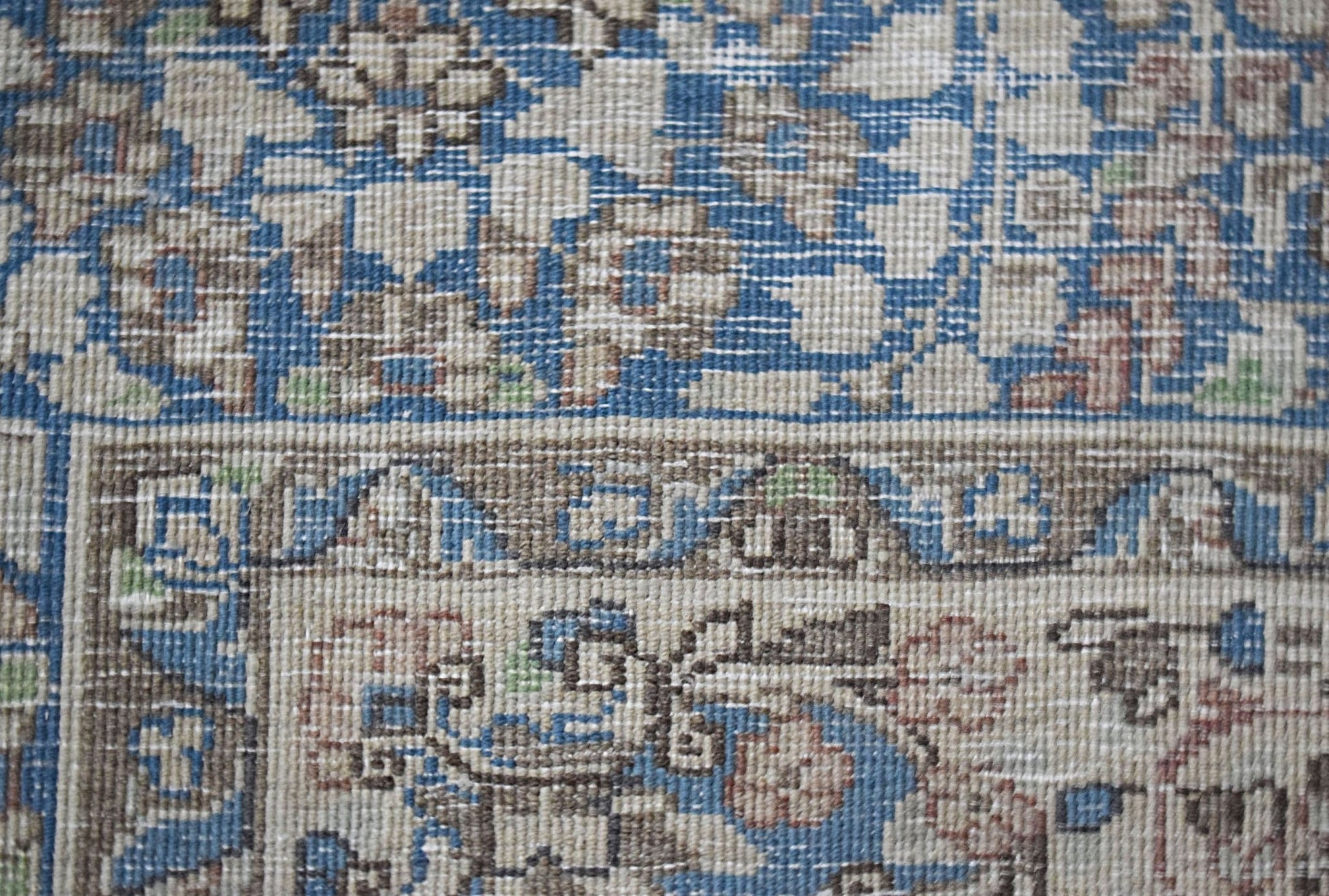 A close-up view of a vintage Persian Kerman rug featuring intricate floral patterns in blue and tan.