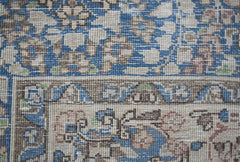 A close-up view of a vintage Persian Kerman rug featuring intricate floral patterns in blue and tan.