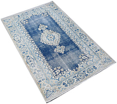 A vintage Persian Kerman rug featuring a central medallion and intricate floral patterns in blue.