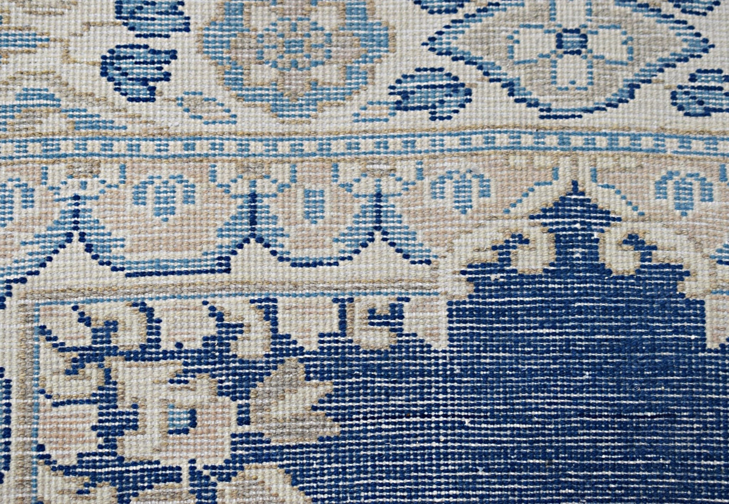 A close-up of a vintage Persian Kerman rug featuring intricate blue and beige floral patterns.