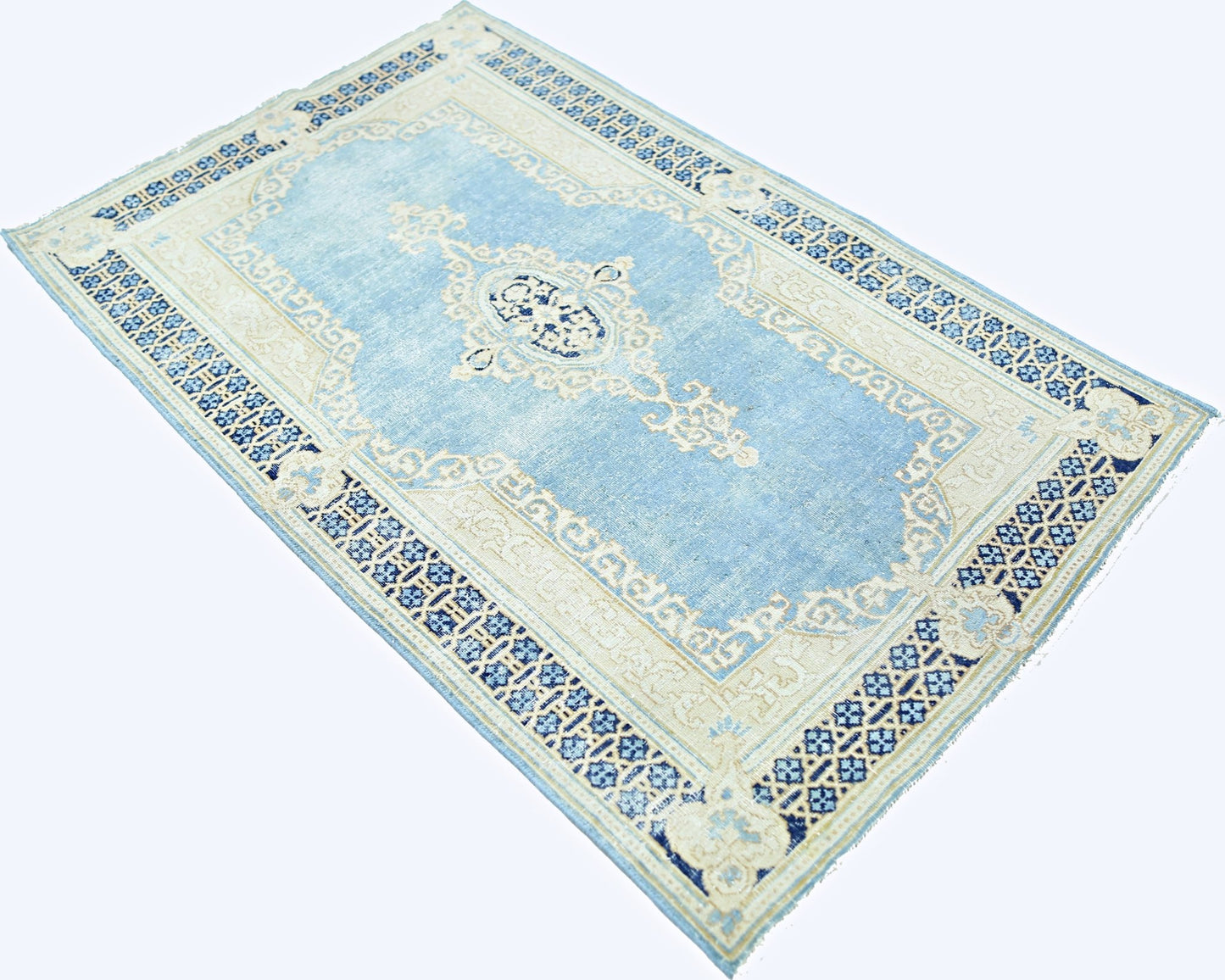 A vintage Persian Kerman rug featuring a central medallion and floral motifs in blue and cream.