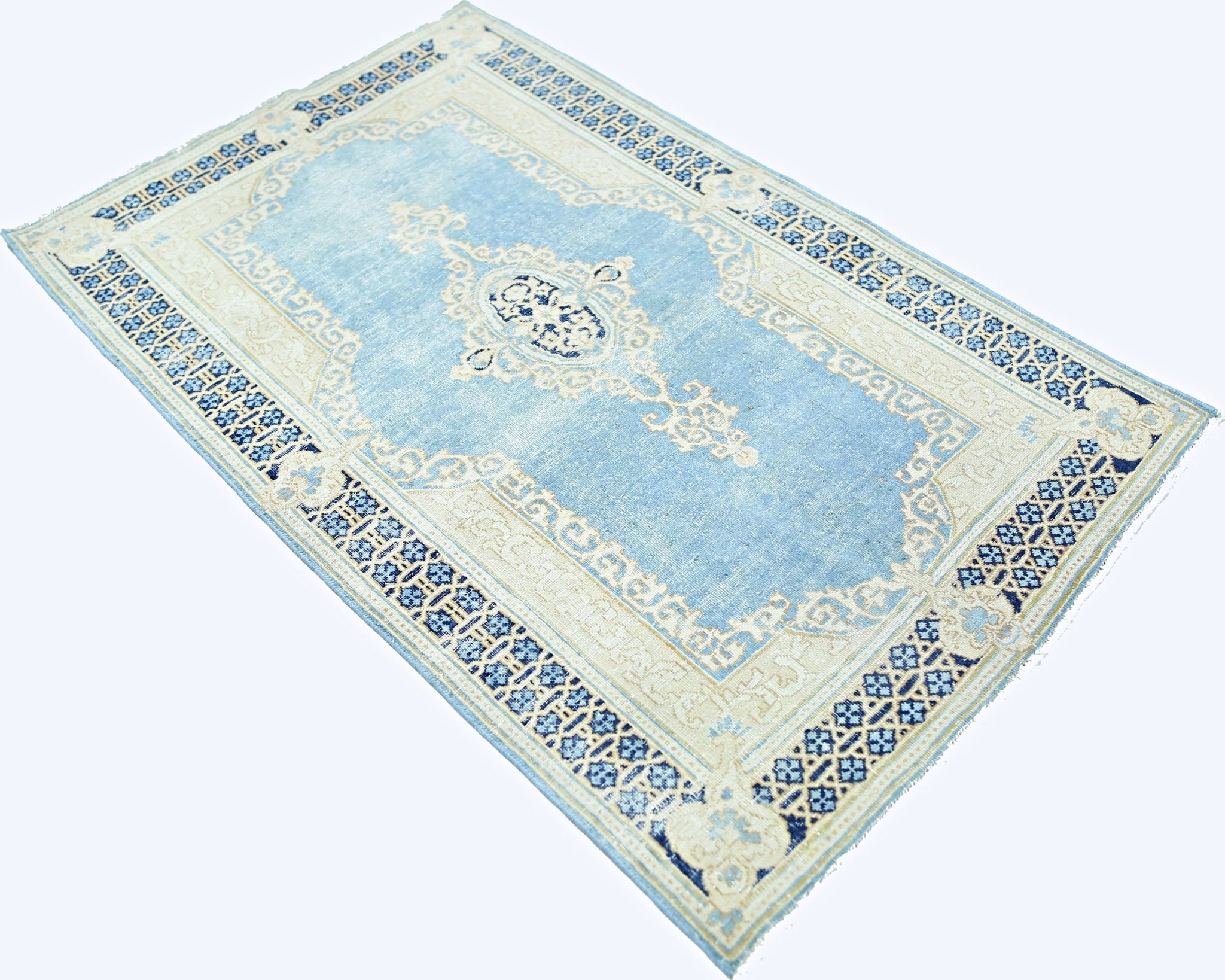 A vintage Persian Kerman rug featuring a central medallion and floral motifs in blue and cream.