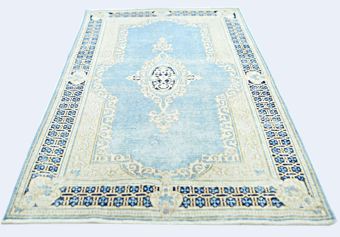 A vintage Persian Kerman rug featuring a central medallion and floral motifs in blue and cream.