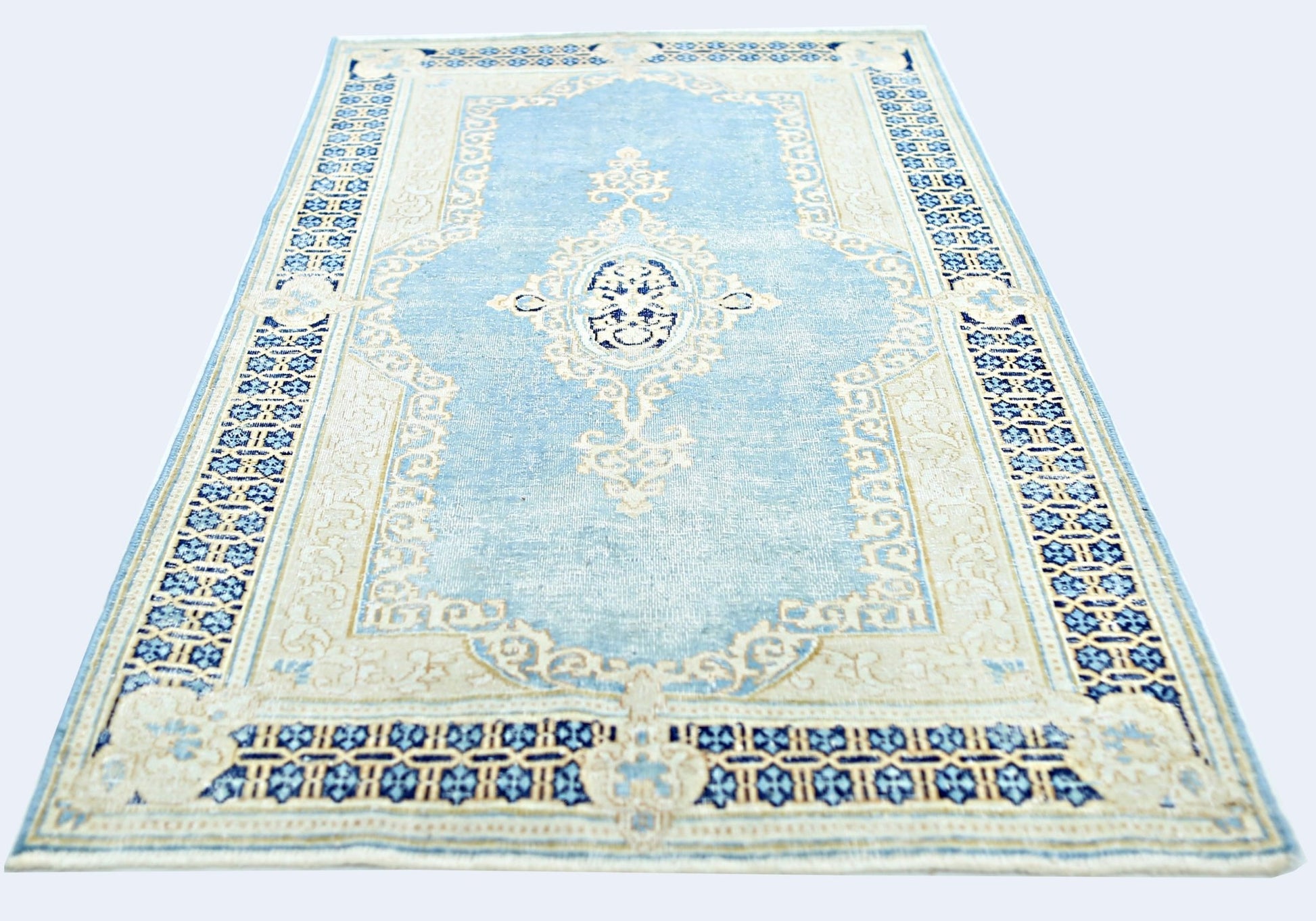 A vintage Persian Kerman rug featuring a central medallion and floral motifs in blue and cream.