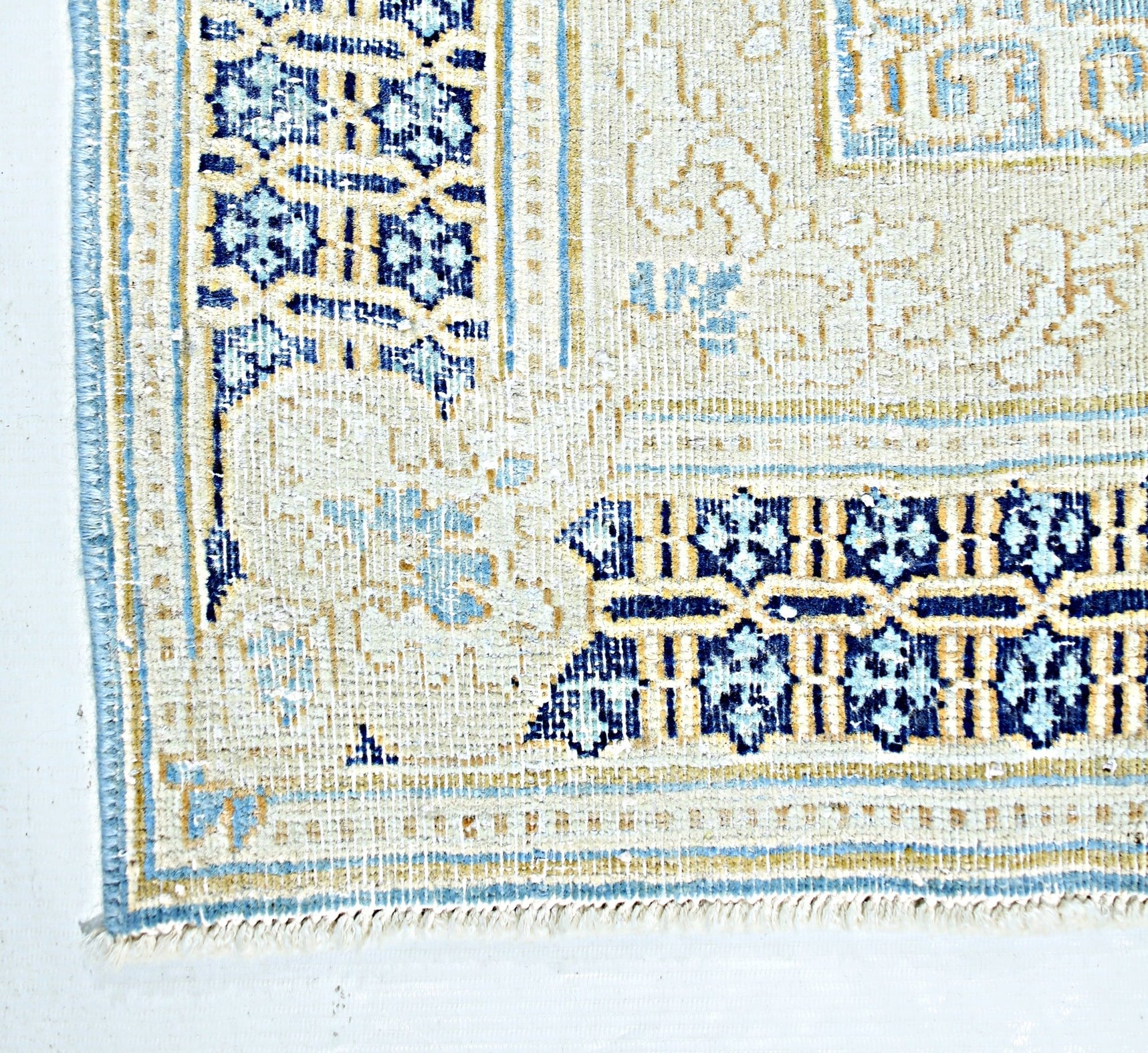 A vintage Persian Kerman rug featuring intricate blue and cream floral patterns and a fringed edge.