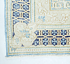 A vintage Persian Kerman rug featuring intricate blue and cream floral patterns and a fringed edge.