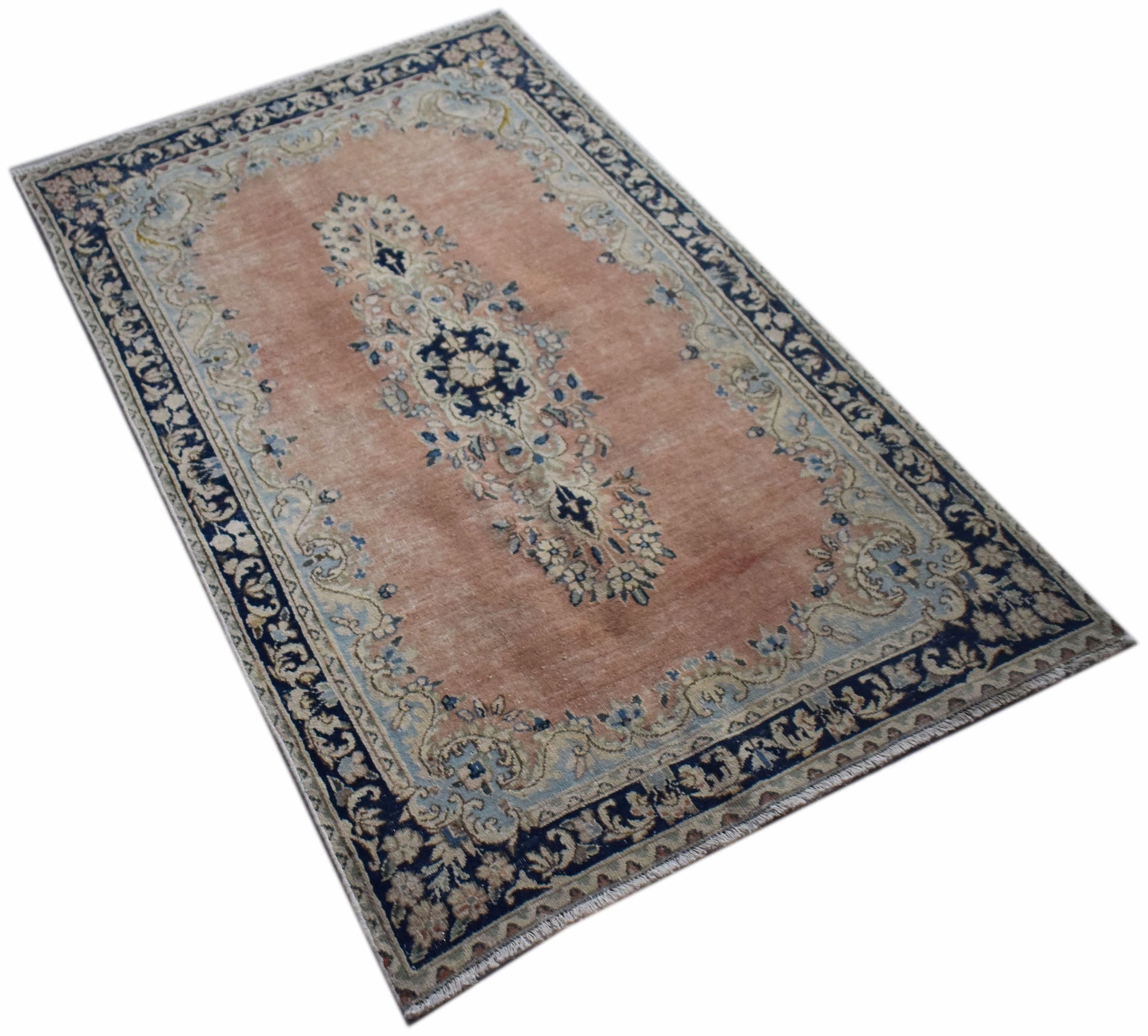 A vintage Persian Kerman rug featuring a central floral medallion on a soft peach field.