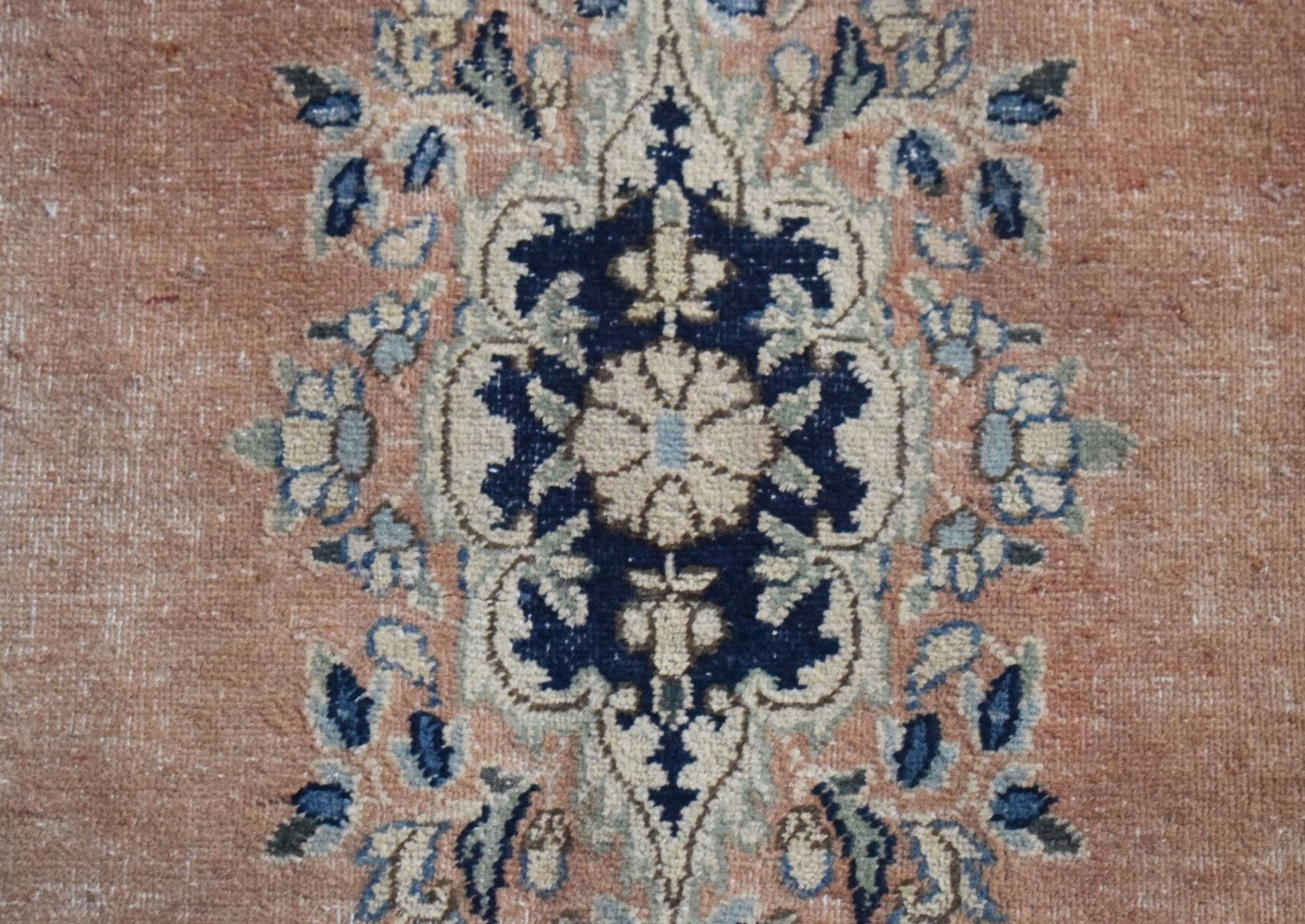 A vintage Persian Kerman rug featuring a detailed floral medallion in blue and cream on a peach base.