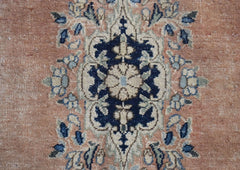 A vintage Persian Kerman rug featuring a detailed floral medallion in blue and cream on a peach base.