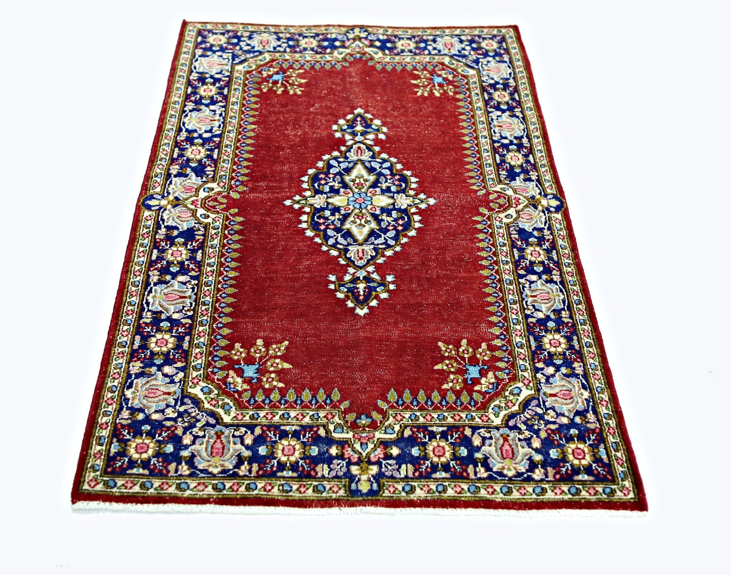 A vintage Persian Kerman rug featuring a central medallion on a red field with blue floral borders.