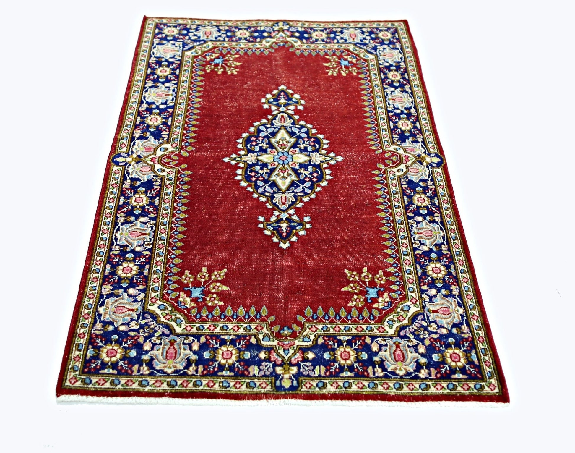 A vintage Persian Kerman rug featuring a central medallion on a red field with blue floral borders.
