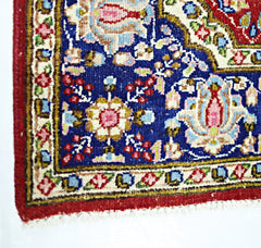 A corner view of a vintage Persian Kerman rug featuring intricate floral patterns on a blue field.