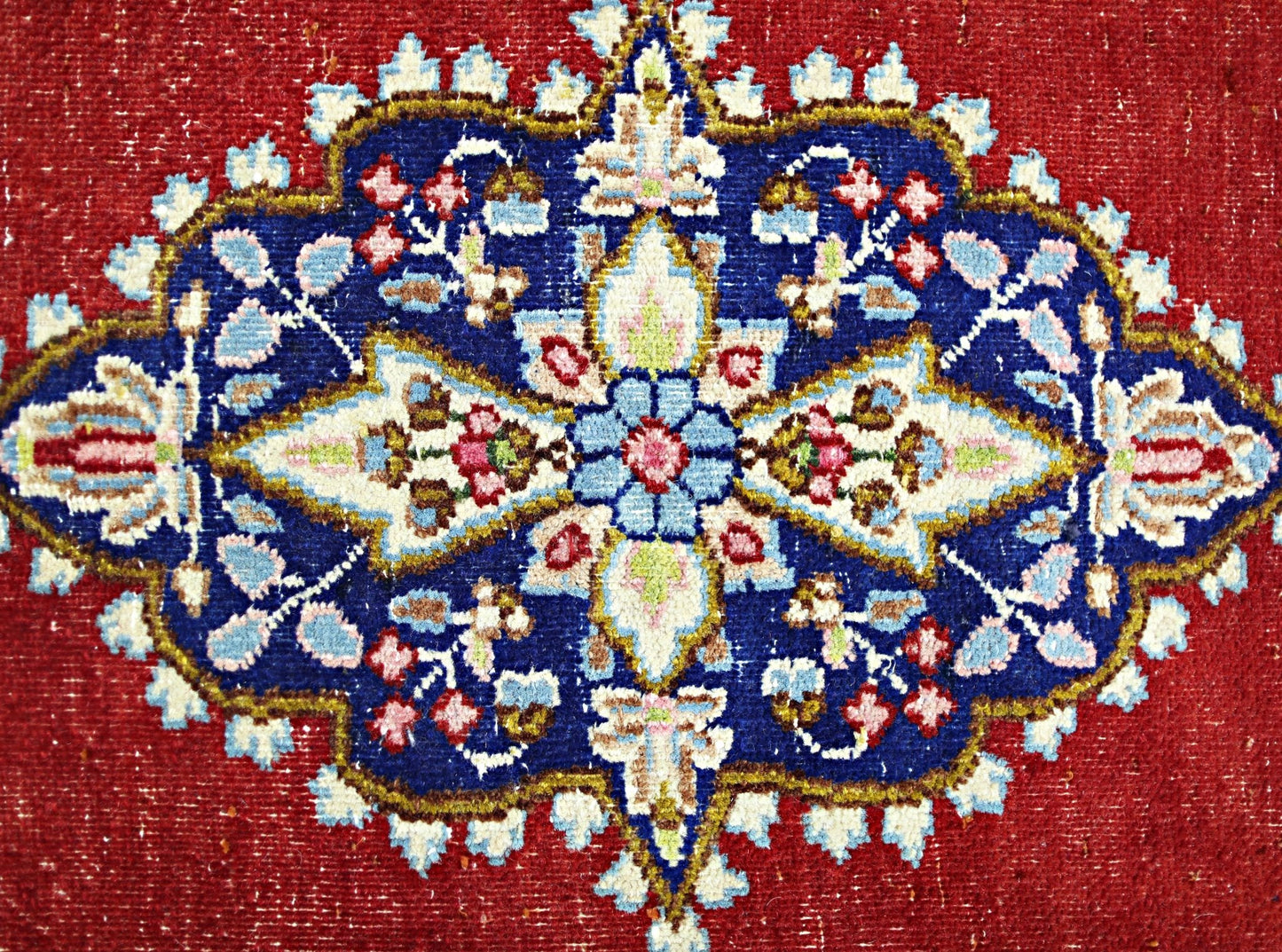 A vintage Persian Kerman rug featuring a detailed floral medallion on a deep red background.