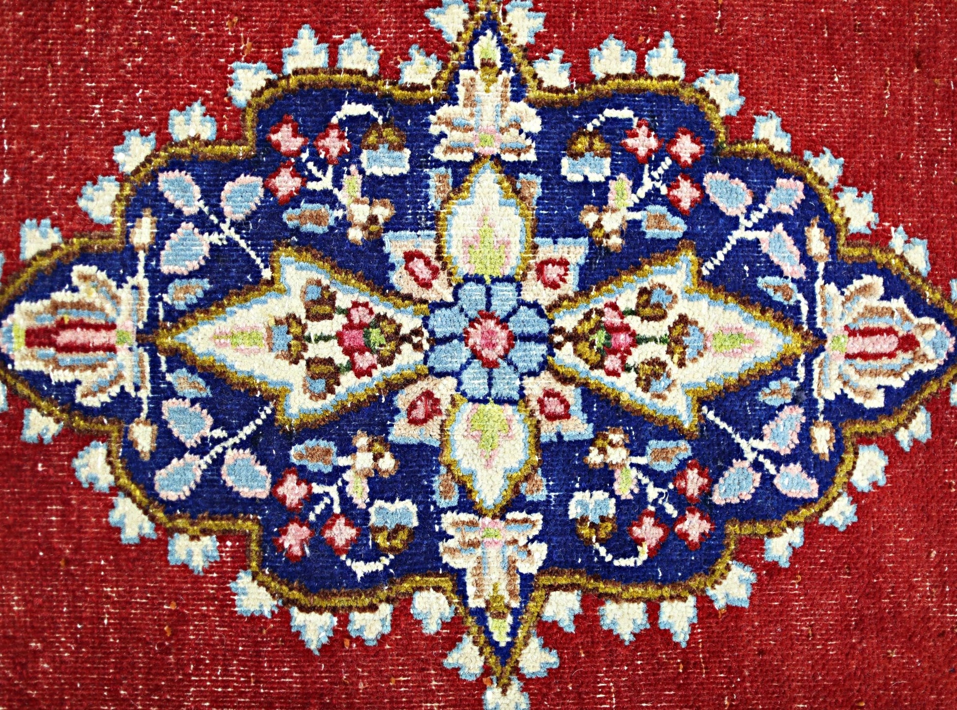 A vintage Persian Kerman rug featuring a detailed floral medallion on a deep red background.