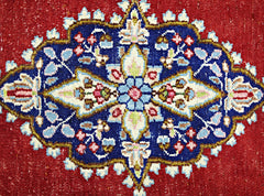 A vintage Persian Kerman rug featuring a detailed floral medallion on a deep red background.