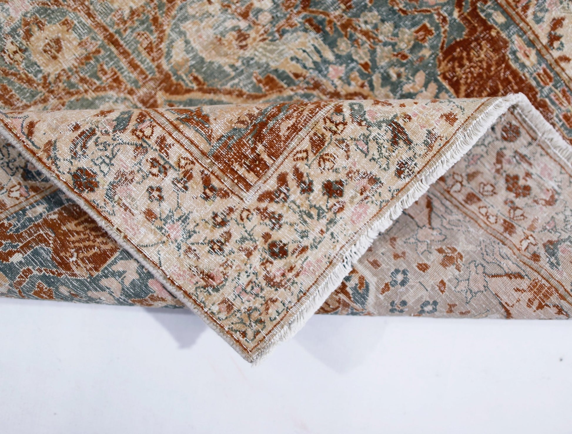 A vintage Persian Kerman rug with a folded corner revealing its intricate floral pattern.