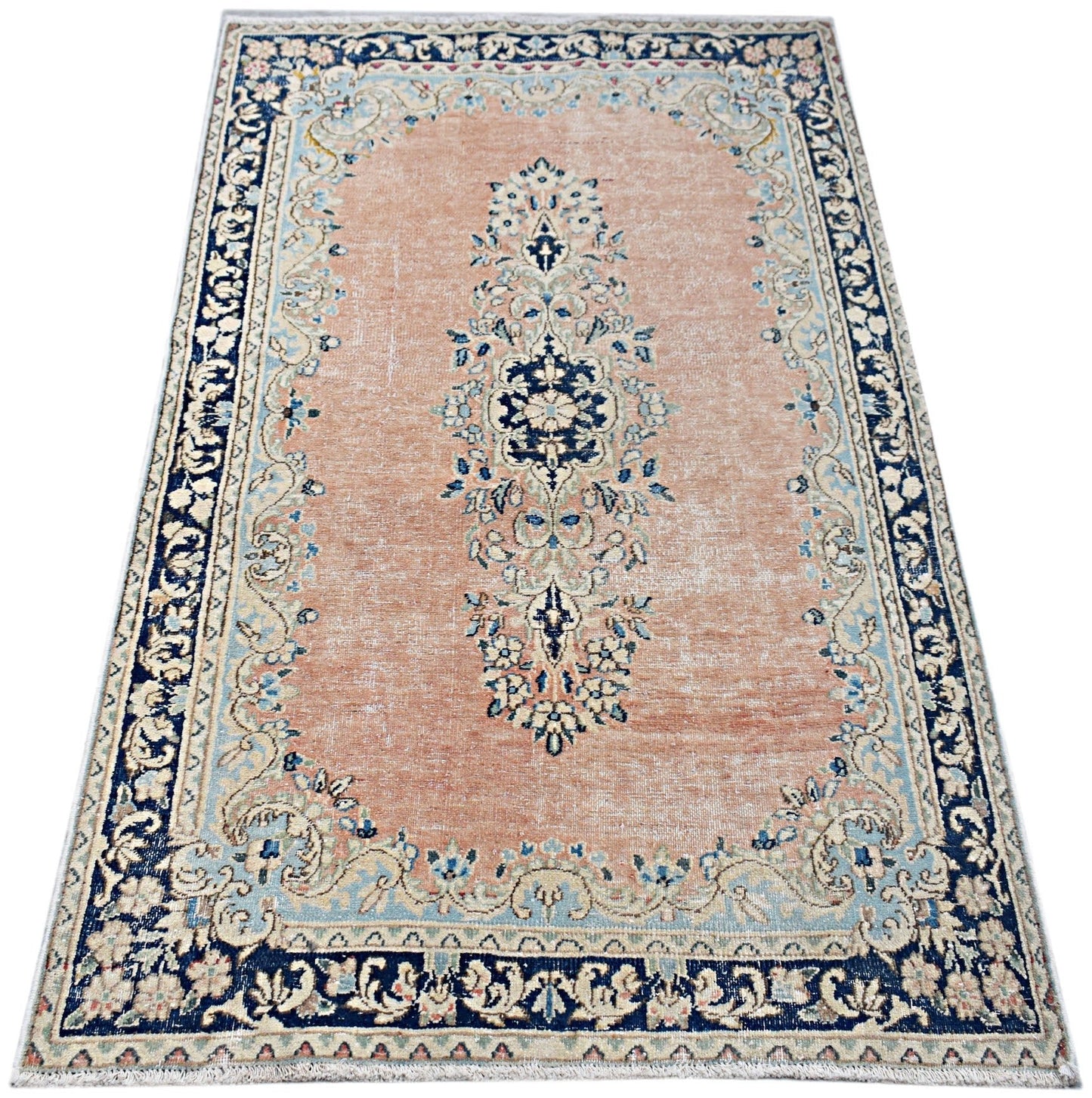 A vintage Persian Kerman rug featuring a central floral medallion on a soft peach field.