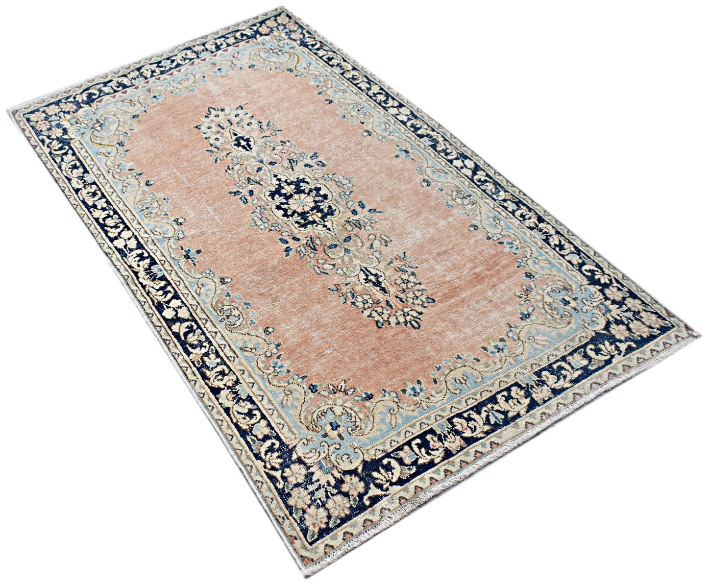 A vintage Persian Kerman rug featuring a central floral medallion on a soft peach field.