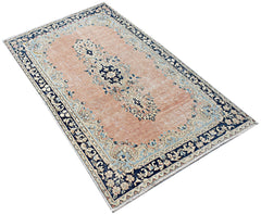 A vintage Persian Kerman rug featuring a central floral medallion on a soft peach field.
