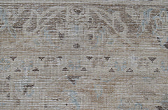 A close-up of a vintage Persian Kerman rug featuring intricate floral patterns in neutral tones.