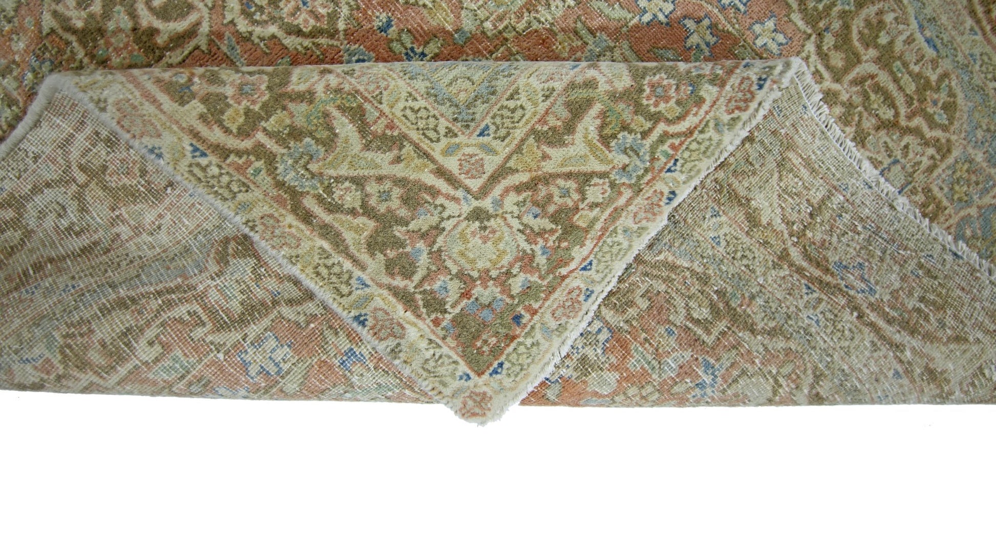 A vintage handmade Persian rug with a folded corner revealing its wool pile and cotton foundation.