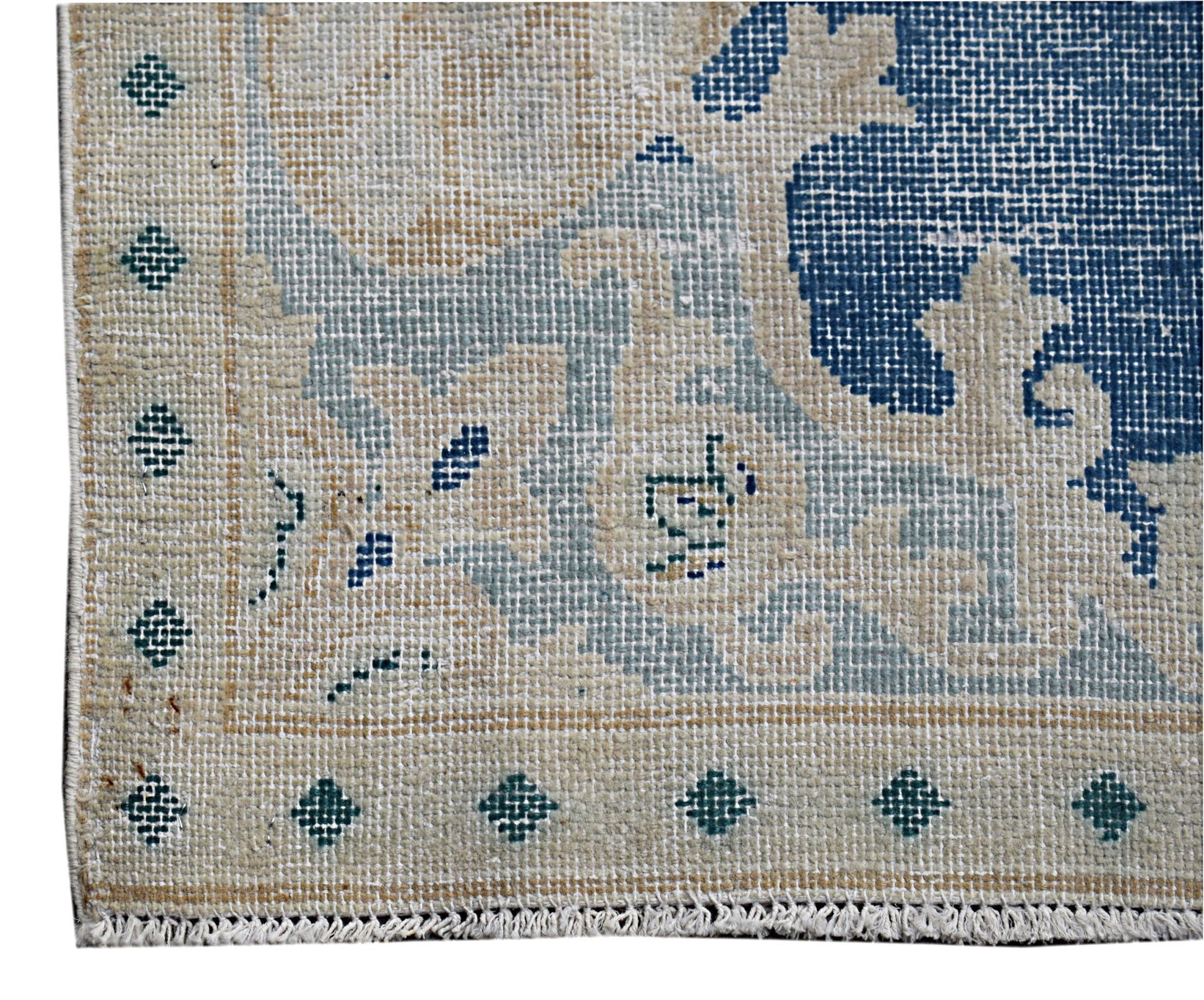 A close-up of a vintage Persian Kerman rug featuring a blue floral pattern on a beige background.