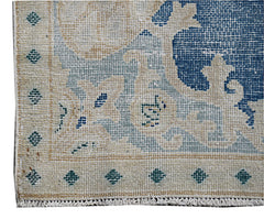 A close-up of a vintage Persian Kerman rug featuring a blue floral pattern on a beige background.