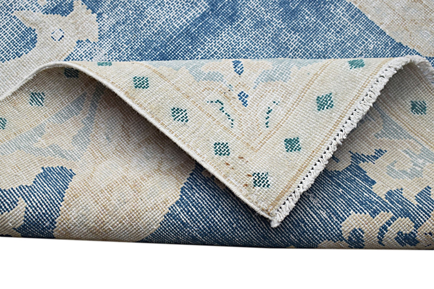 A vintage Persian Kerman rug featuring a blue and cream floral pattern with a folded corner.
