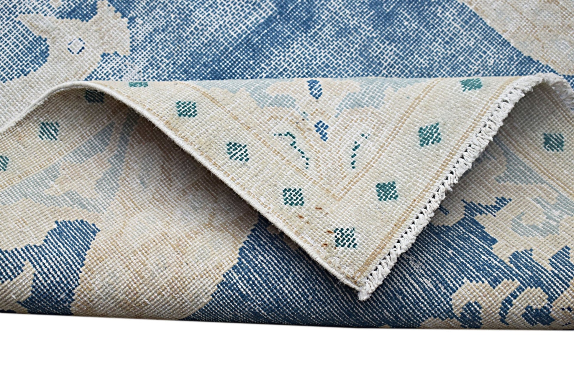 A vintage Persian Kerman rug featuring a blue and cream floral pattern with a folded corner.